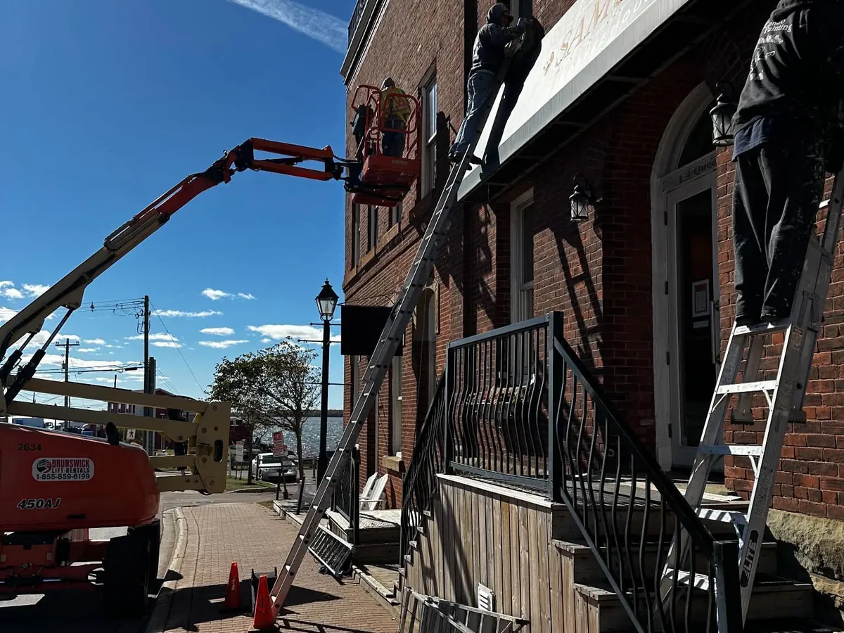 A crew on a boom lift and ladders working on the awning at Harbour Terrace in Summerside